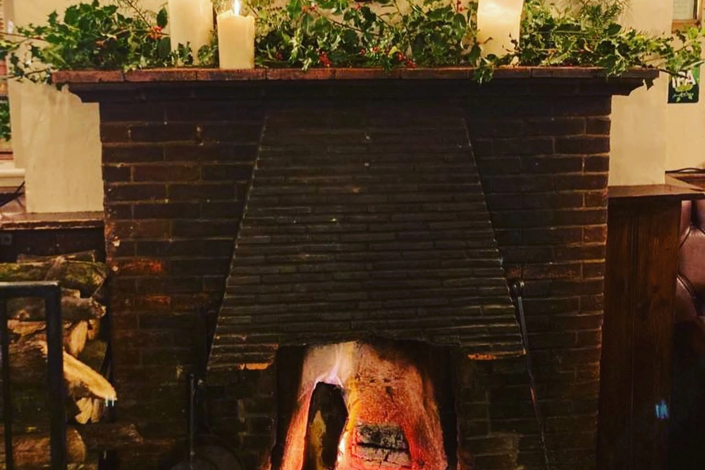 Traditional open fireplace decorated with greenery and candles inside The Hare Arms